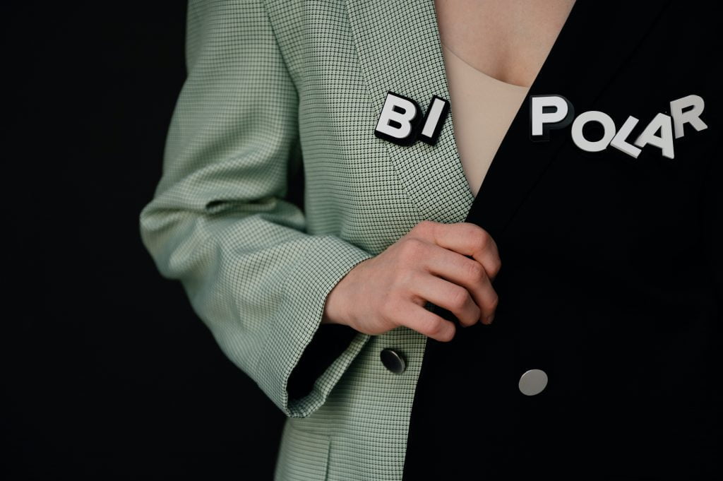 A person wearing a blazer that's half green half black with the word bipolar spelled.