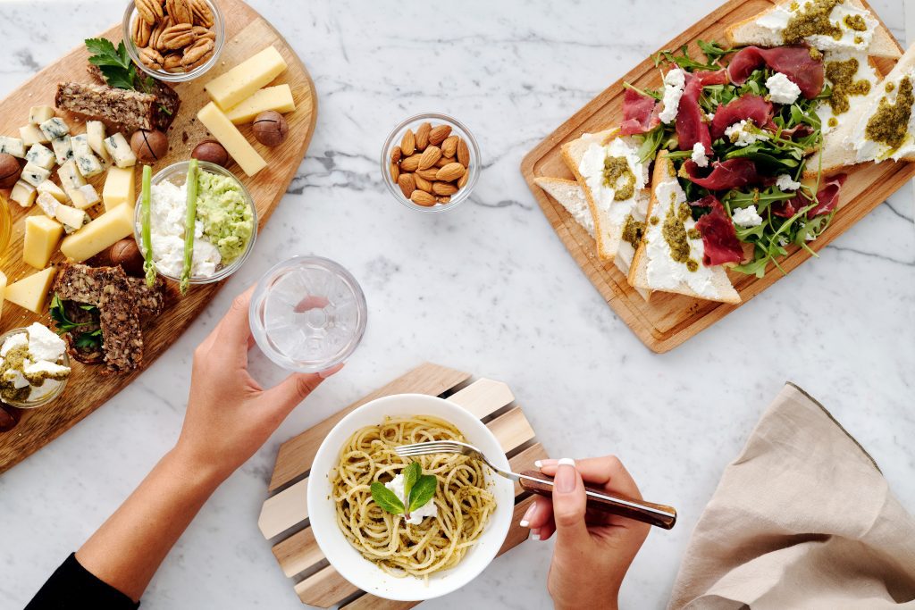 Three plates of food with a person golding a fork in one hand and a drink in the other.