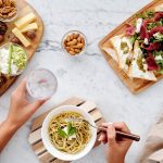Three plates of food with a person golding a fork in one hand and a drink in the other.