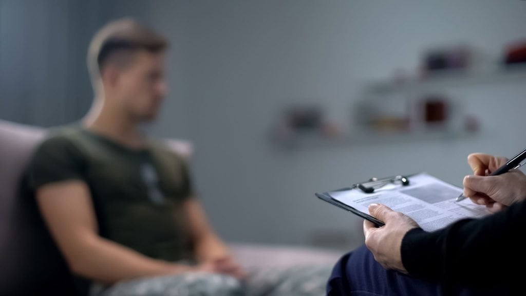 Therapist taking notes while talking to someone in the background