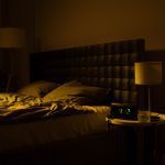 Empty bed in a dark room with a clock that reads 4:12.