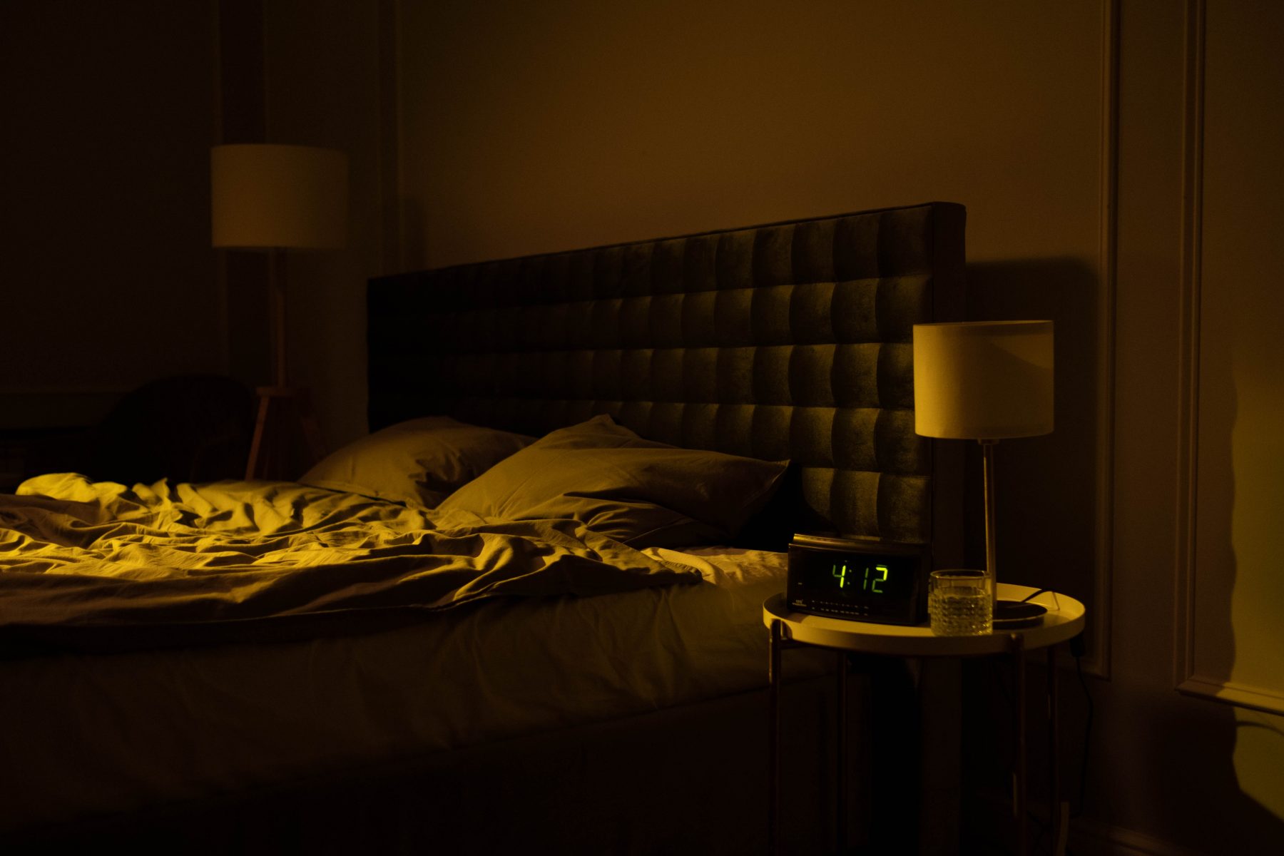 Empty bed in a dark room with a clock that reads 4:12.