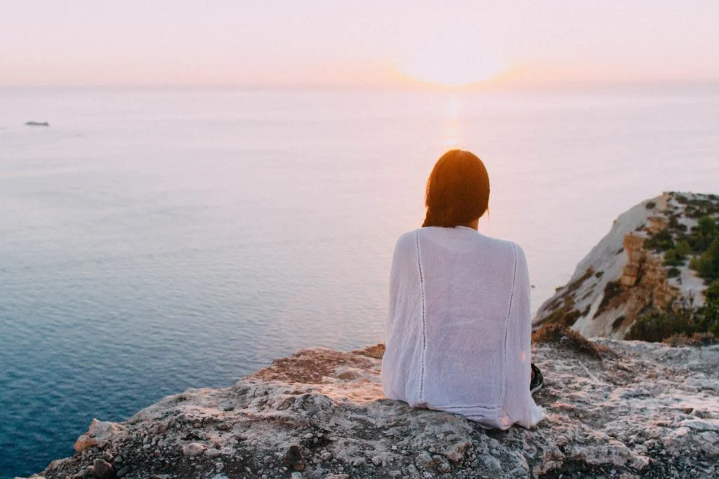 Woman sitting on rocks facing the sea.