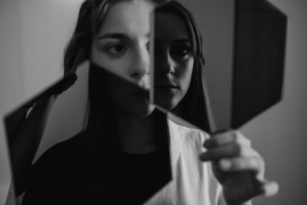 Black and white picture of a woman holding looking at mirrors.