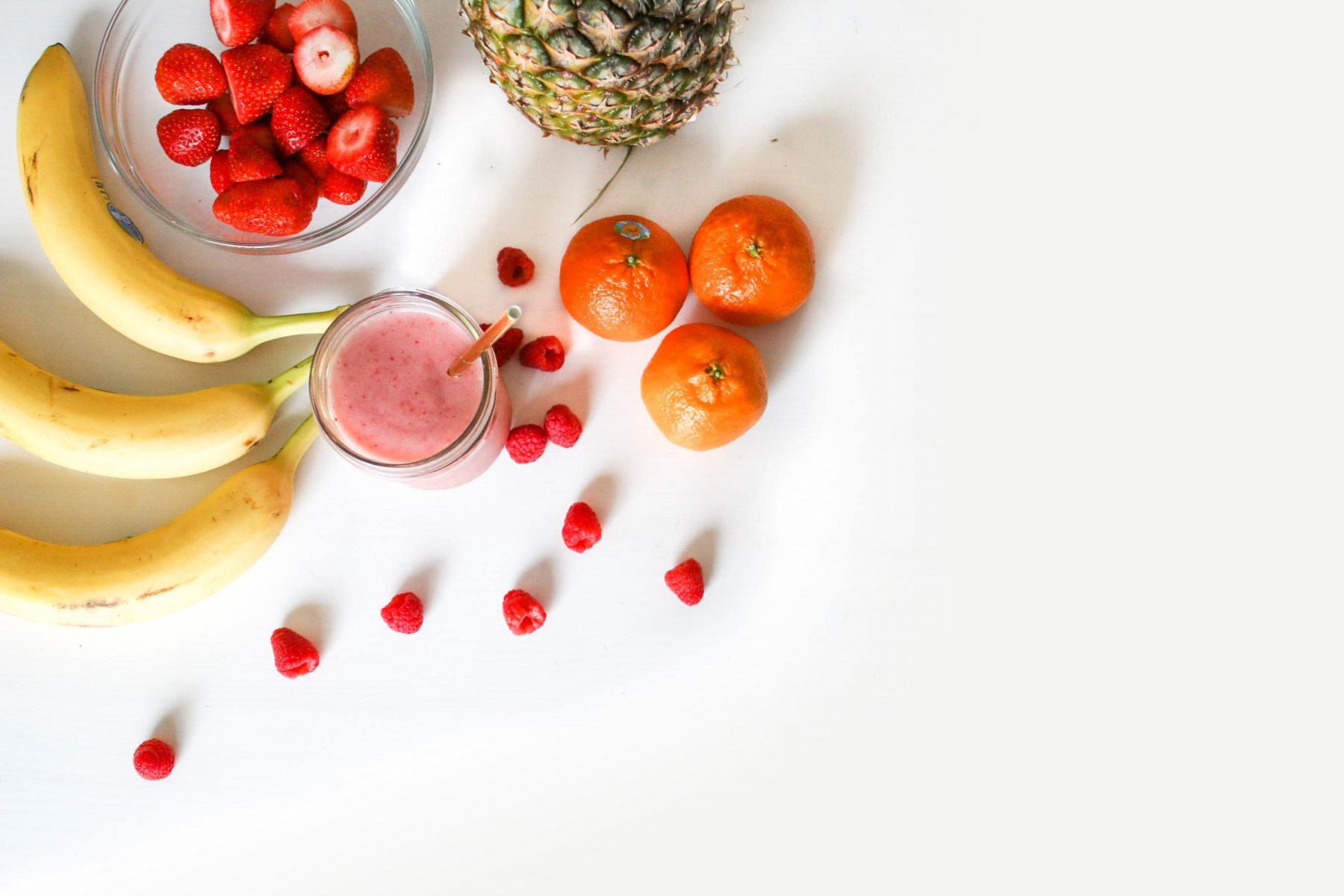 Oranges, bananas, strawberries, berries, and a pineapple with a white background.