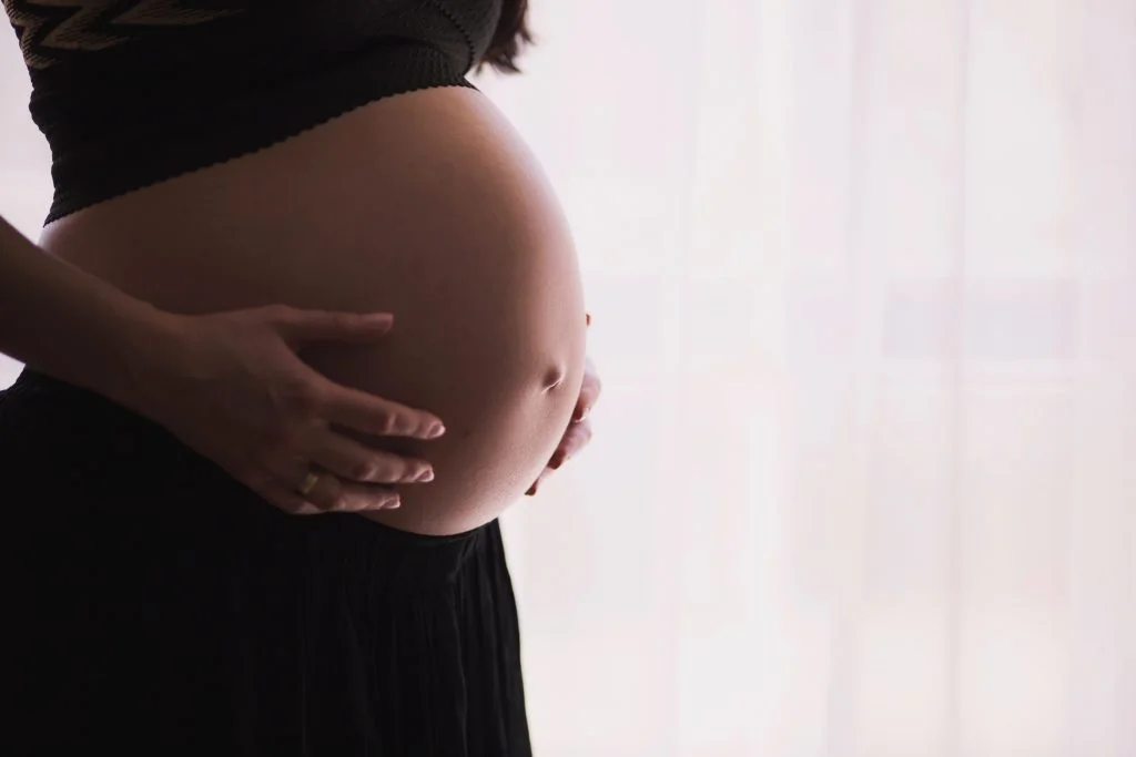 A pregnant woman with her arms around her belly.