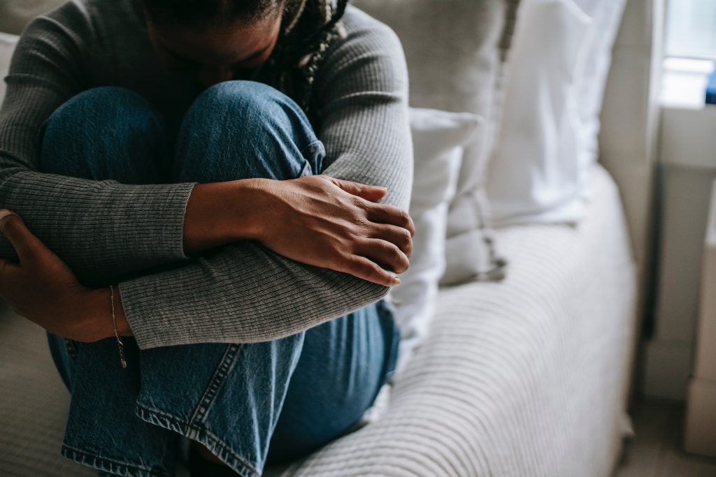 Person sitting on a bed while hugging their legs to their chest seemingly having a nervous breakdown.